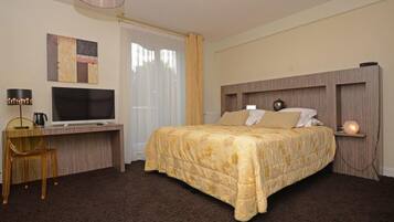 Ein Hotelzimmer mit einem Bett, einem Schreibtisch mit Fernseher, einem Sessel und einer Lampe.