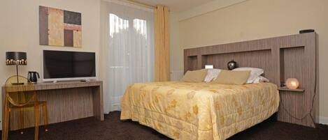 Ein Hotelzimmer mit einem Bett, einem Schreibtisch mit Fernseher, einem Sessel und einer Lampe.