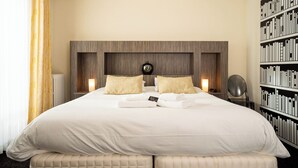 A large bed with white linens, two bedside lamps, a clock on the wall, and a bookshelf to the right. - Hotel la Réserve (Gerardmer)