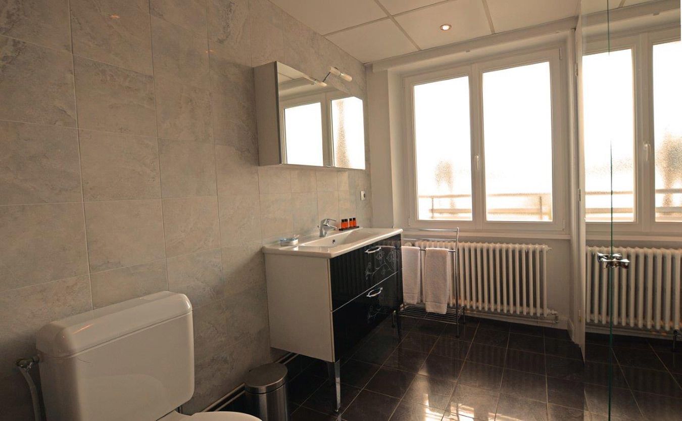 Une salle de bain moderne équipée de toilettes, d’un lavabo avec un miroir et d’une fenêtre laissant entrer la lumière naturelle.