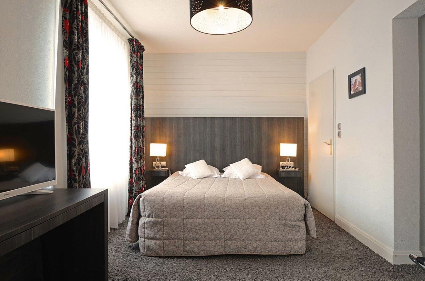 A hotel room with a large bed, two bedside lamps, a flat-screen TV on a stand, and a ceiling light fixture.
