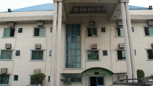 Un edificio de varios pisos con fachada simétrica, unidades de aire acondicionado y una entrada central con arco verde.