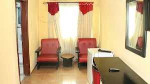Una habitación pequeña con dos sillas rojas, una mesita y un armario blanco.