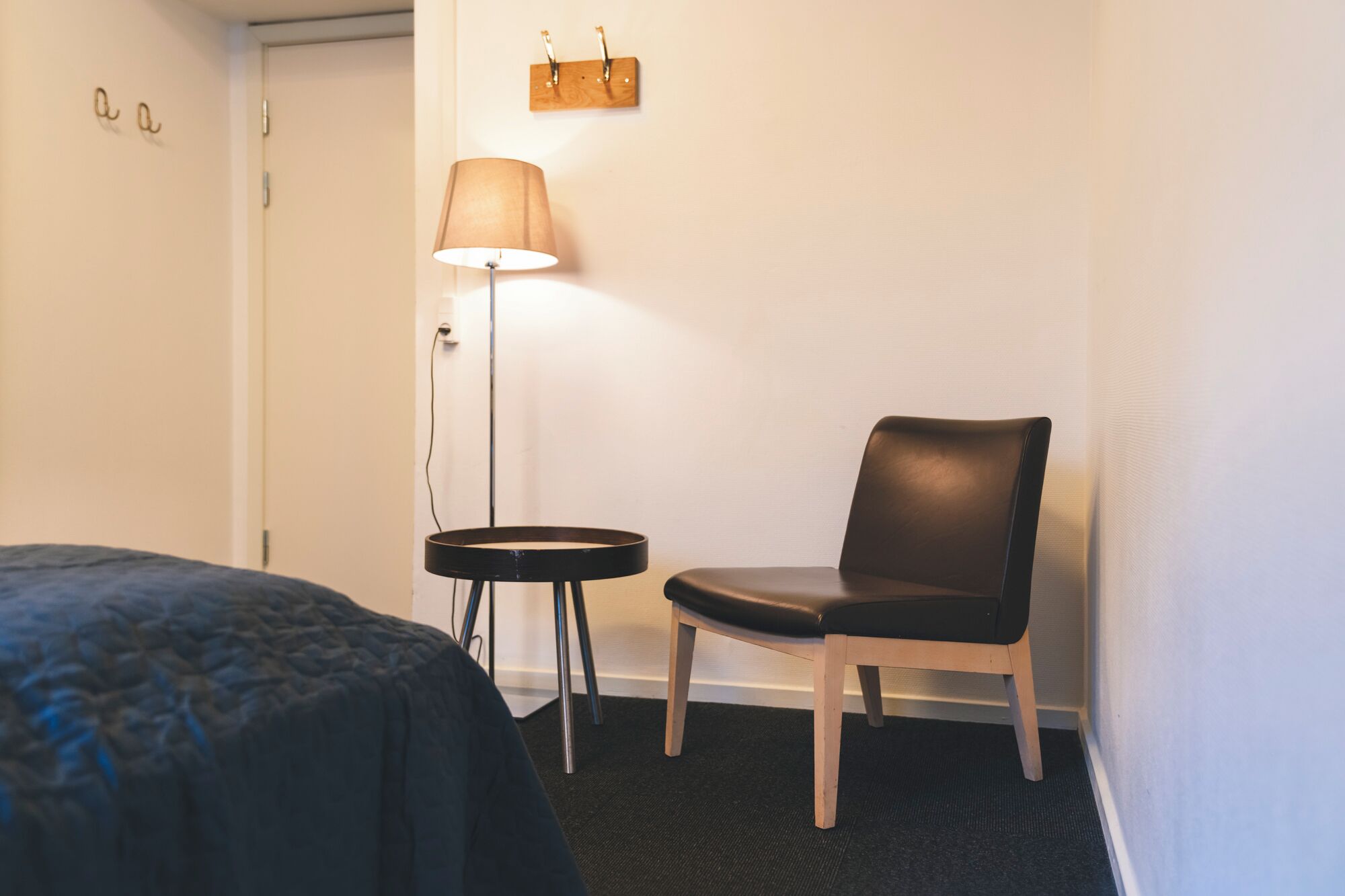 A hotel room with a bed, a chair, a small table, and a floor lamp.