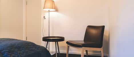 A hotel room with a bed, a chair, a small table, and a floor lamp.