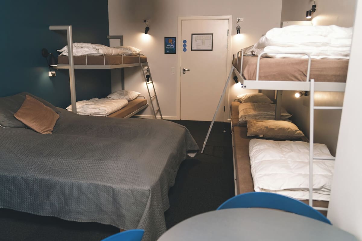 A dormitory room with bunk beds, a desk, and a door with a poster.