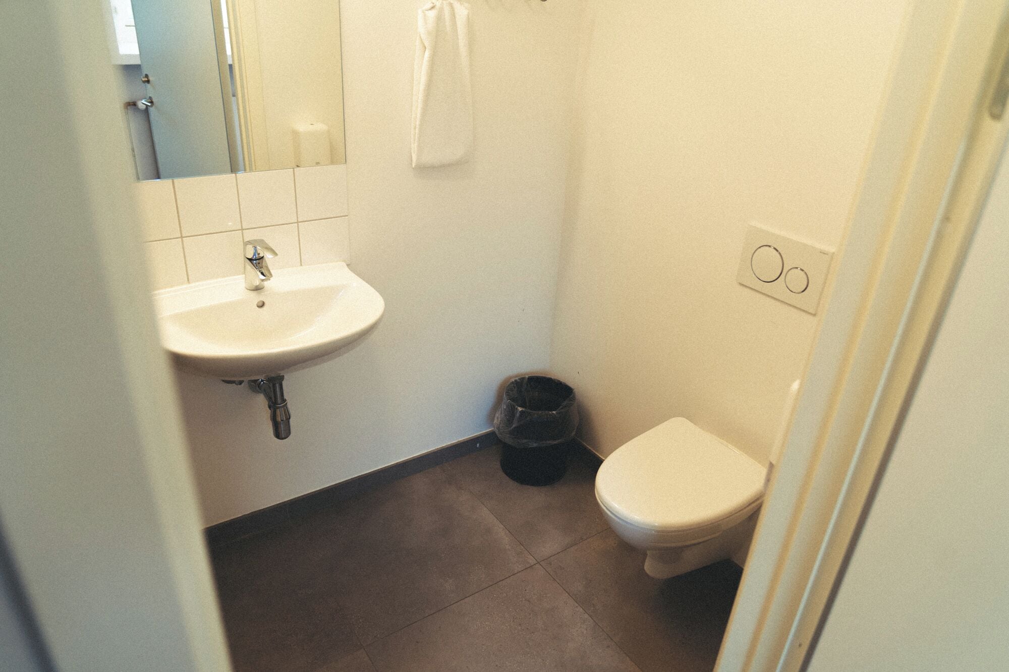 Une petite salle de bain avec un lavabo blanc, des toilettes et une poubelle.