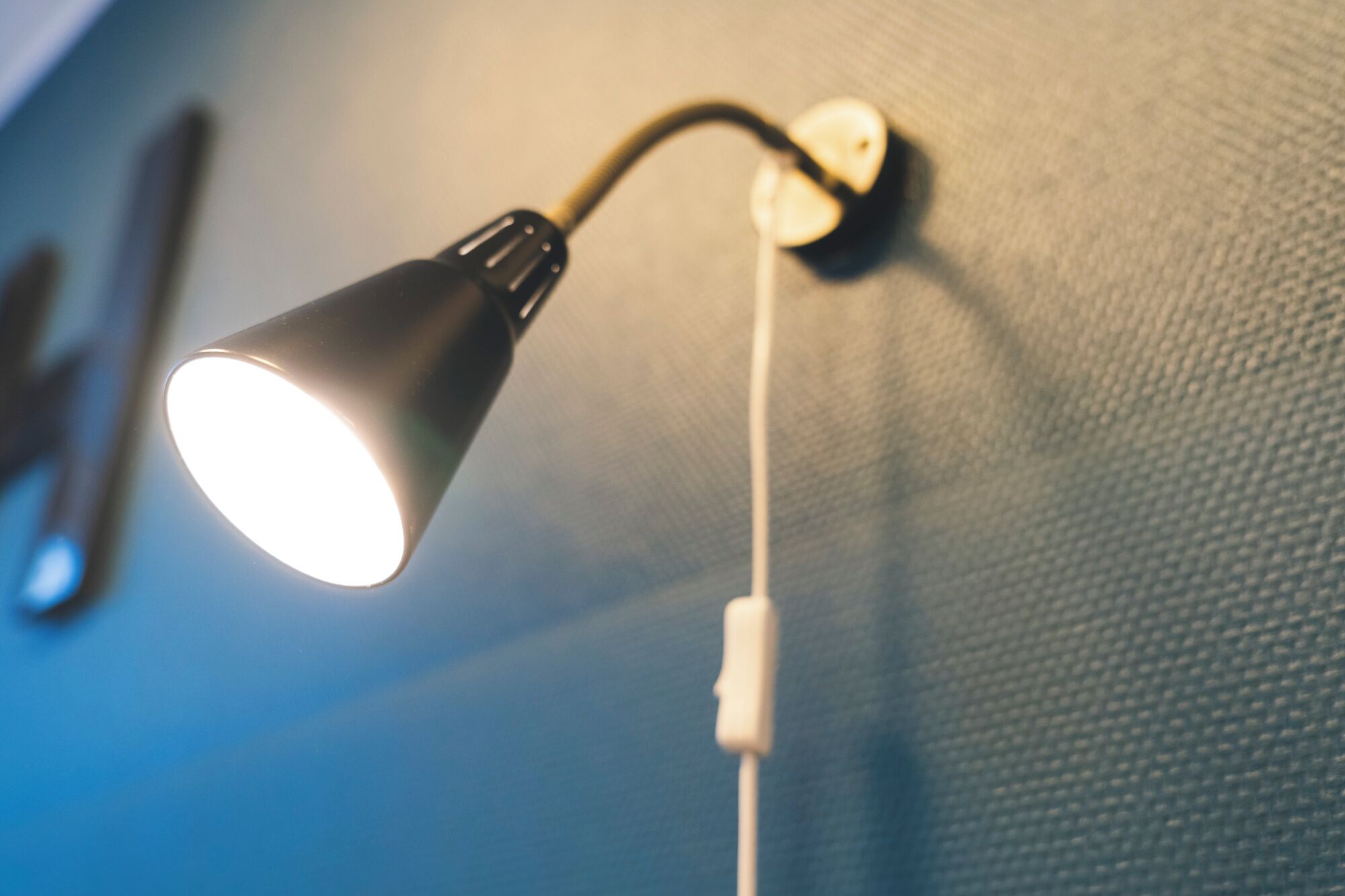 A wall-mounted lamp with a white cord plugged into a wall socket.