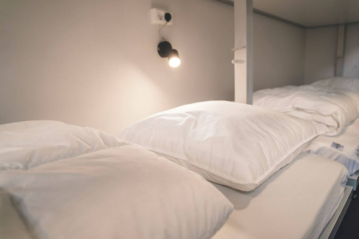 A single bed with white bedding and a wall-mounted light fixture.