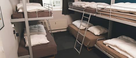 A dormitory room with bunk beds, a radiator, a window with curtains, and a door.