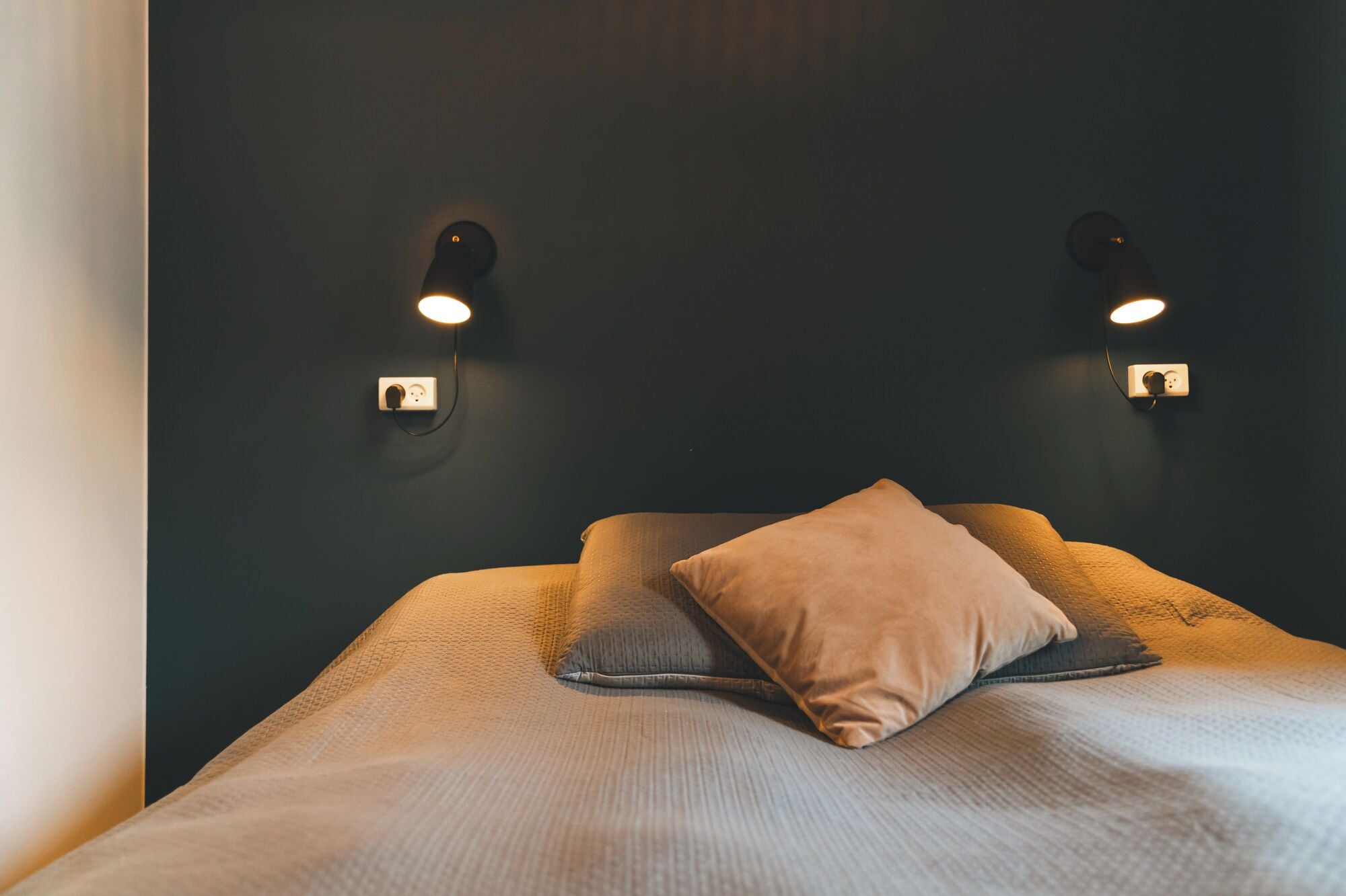 Un letto con due cuscini e due luci fissate al muro.