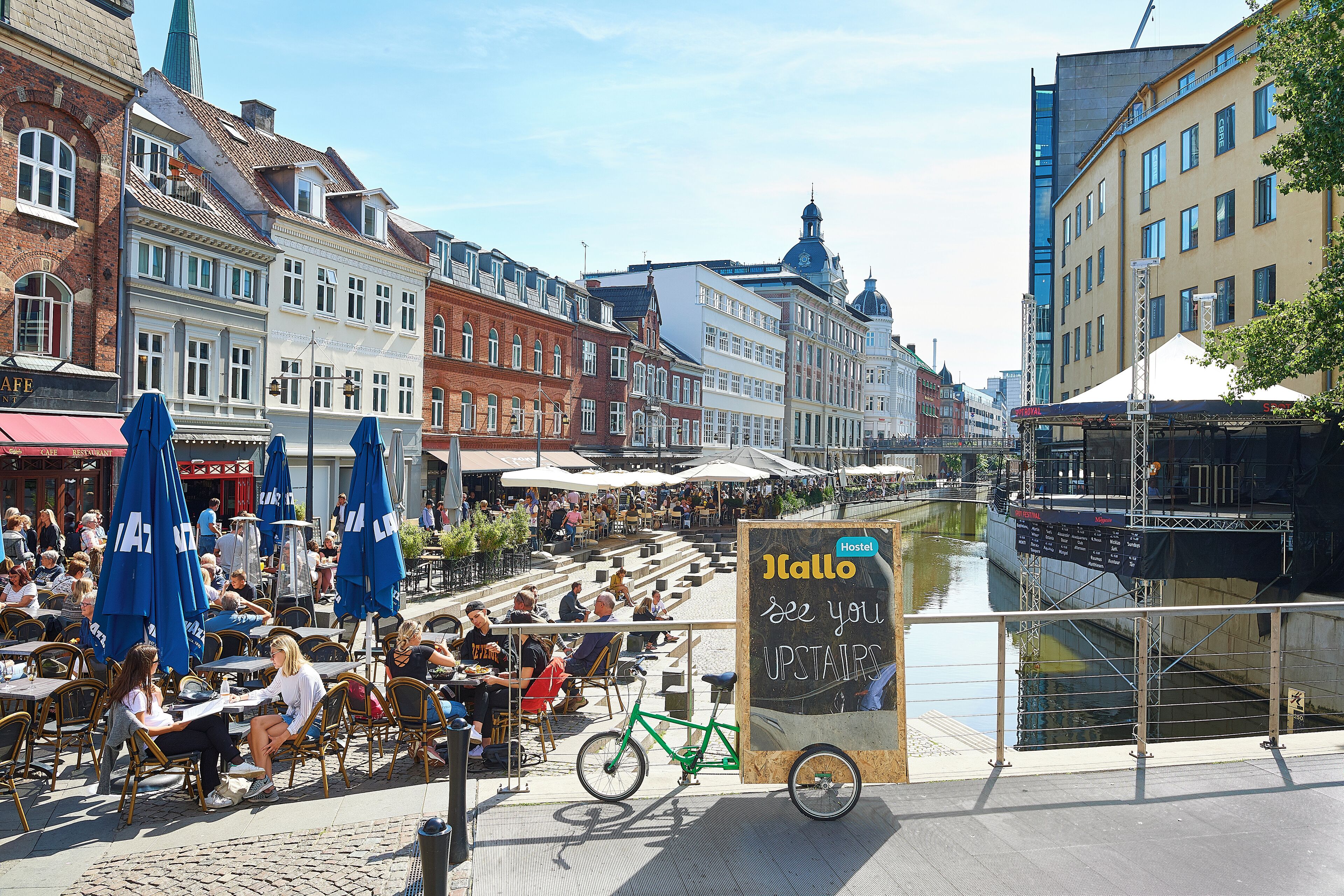 A bustling outdoor café with tables and chairs, a bicycle, and a signboard.