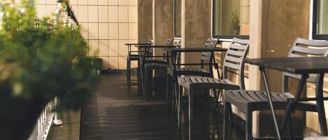 A covered outdoor seating area with tables and chairs, a tiled wall, and a potted plant.