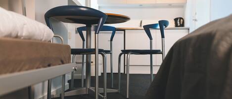 A compact room with a bed, a small kitchenette, and two chairs.