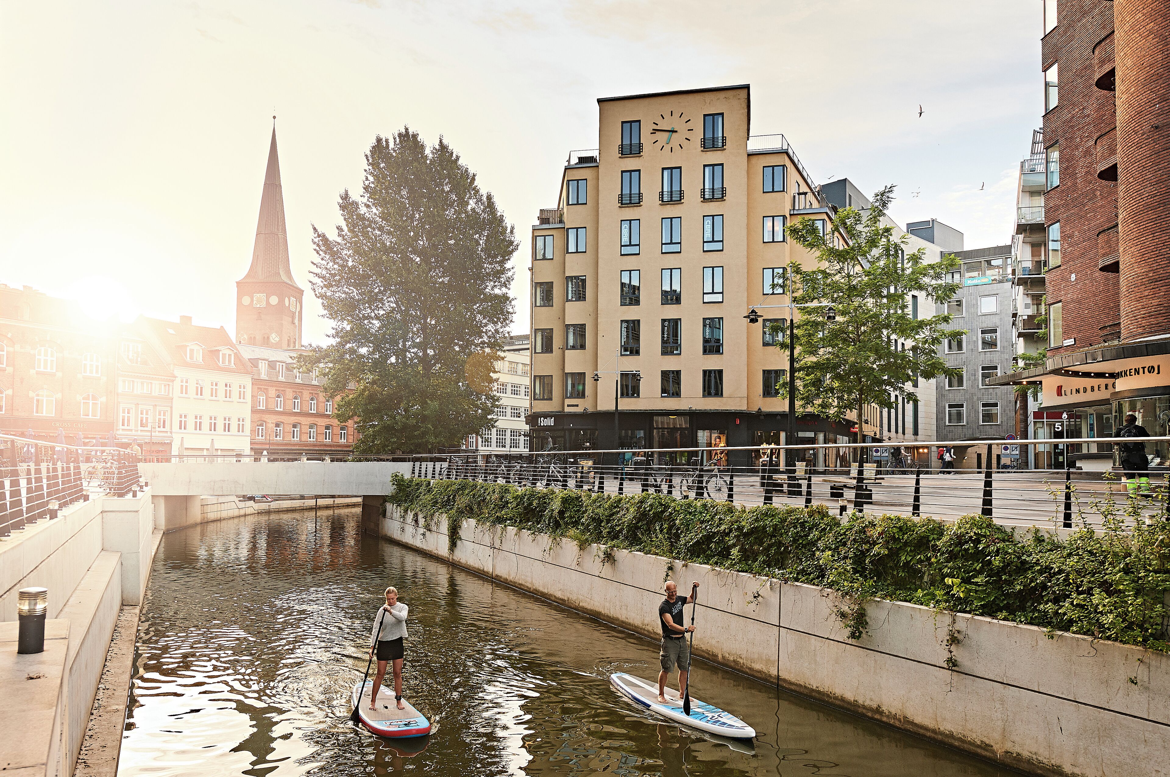 Een gracht met twee peddelplanken, een brug en gebouwen op de achtergrond.