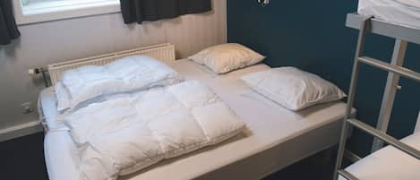 A single bed with white bedding, a window with curtains, a radiator, and a wall-mounted lamp.