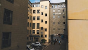 Un edificio de varios pisos con un cartel que indica 'DANHOSTEL', un albergue juvenil. Se ven varios coches aparcados y algunas personas en la calle.