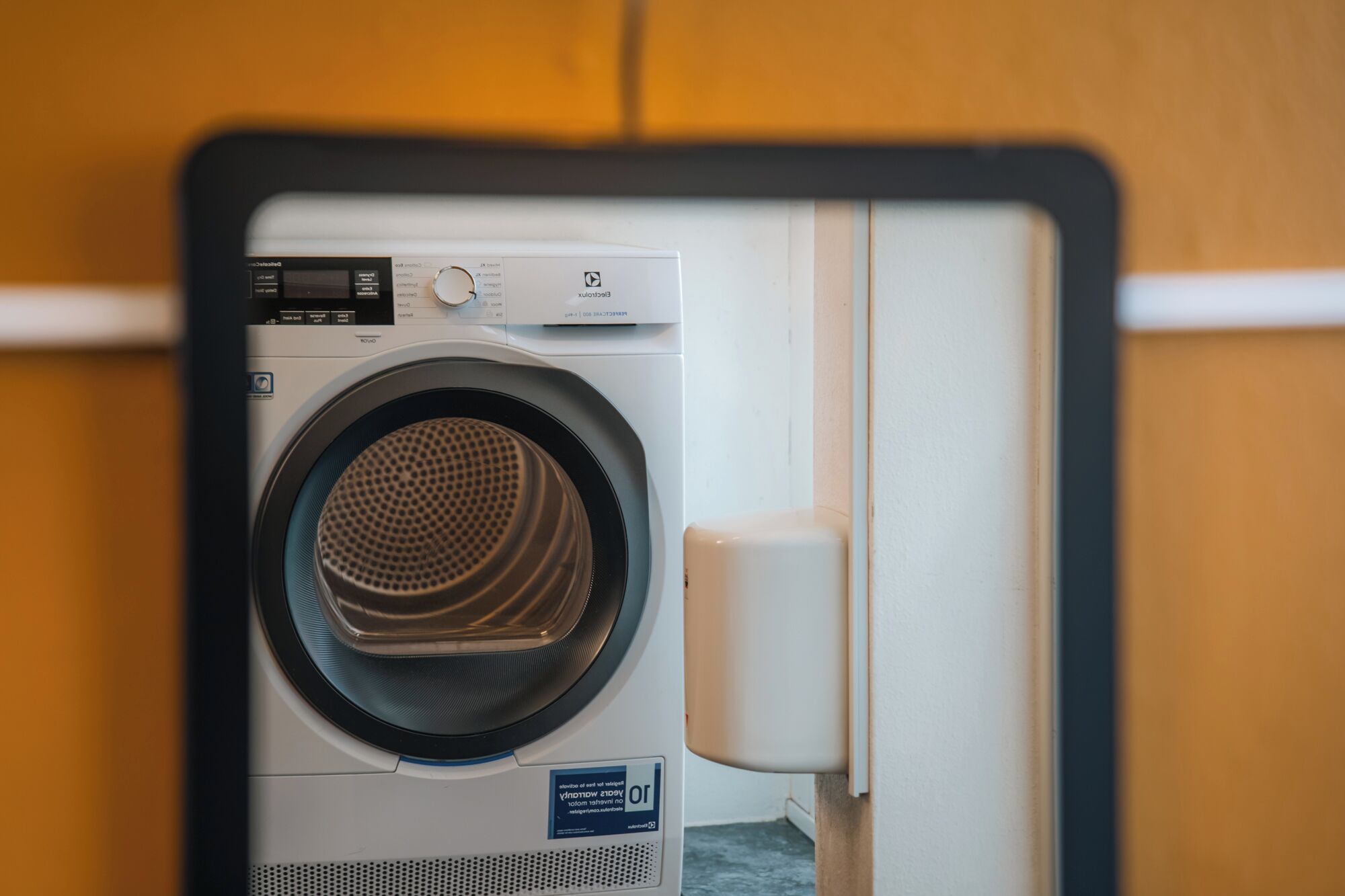 A front view of a washing machine in a room with a wooden wall and a white door.