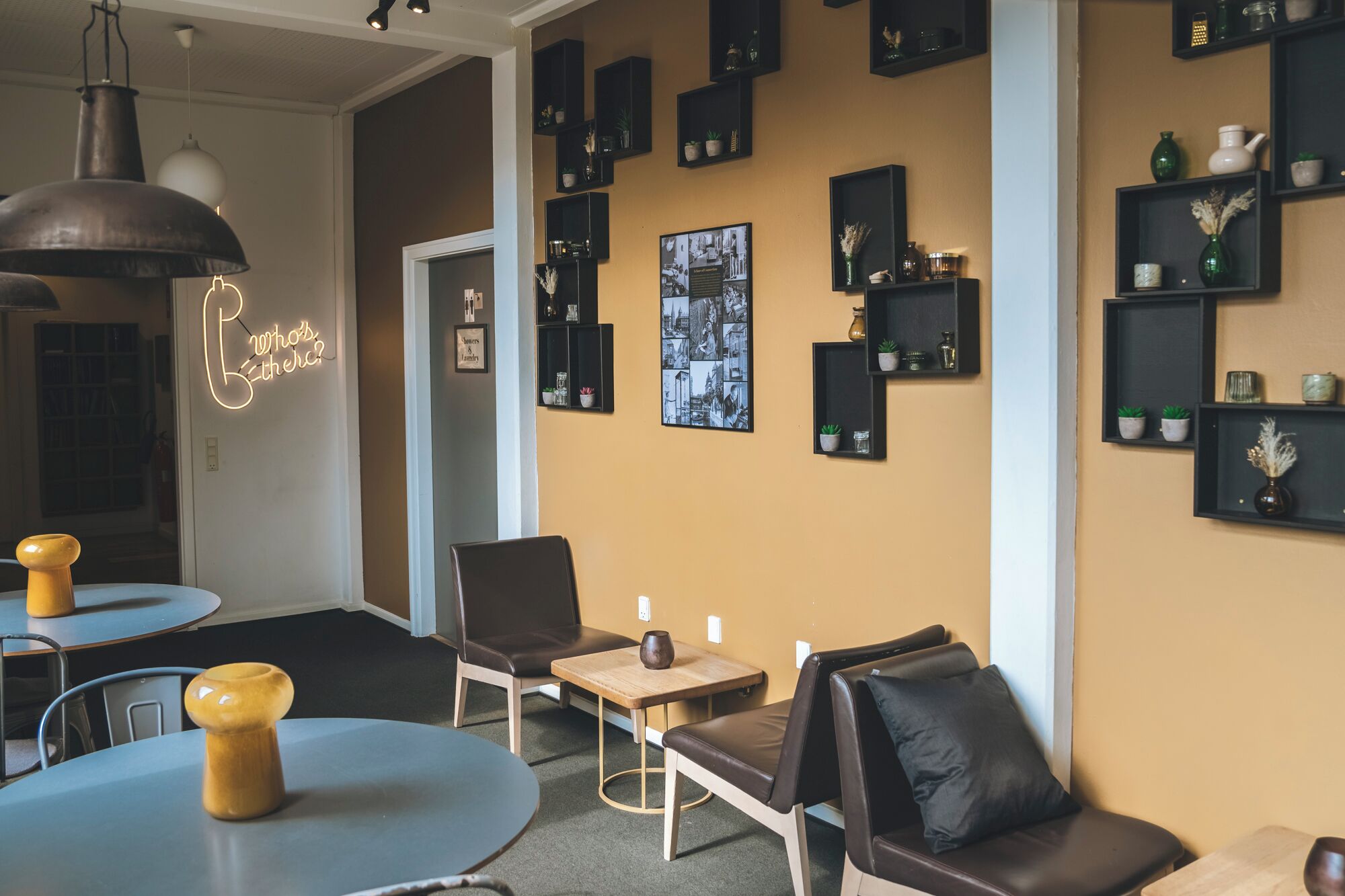 A modern interior with a round table, two chairs, a small wooden table, and a bench. There are multiple black shelves with decorative items and a neon sign on the wall.