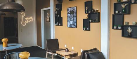 A modern interior with a round table, two chairs, a small wooden table, and a bench. There are multiple black shelves with decorative items and a neon sign on the wall.