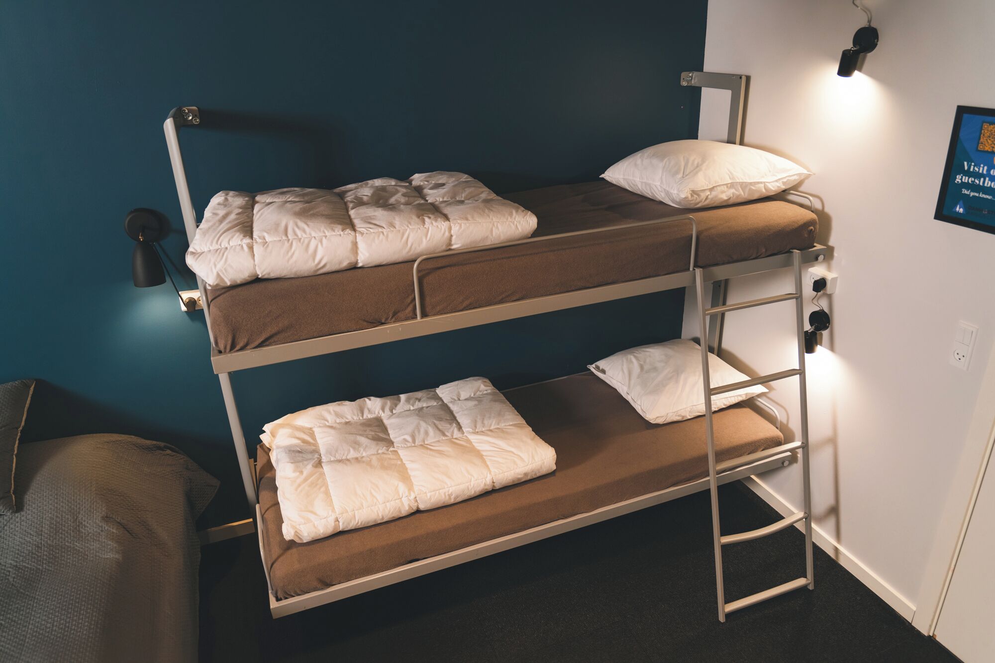 A bunk bed with two levels, each with a pillow and a blanket. There is a ladder on the side for access to the upper bunk.