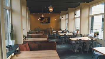 A restaurant interior with wooden tables and benches, large windows, and hanging pendant lights.