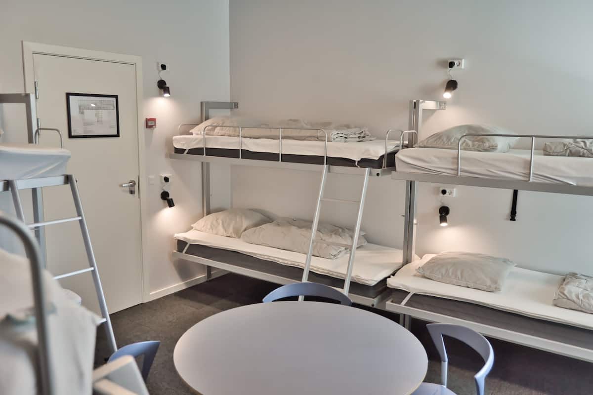 A dormitory room with bunk beds, a white door, a framed map, and a round table with chairs.