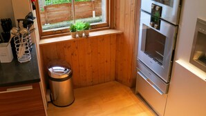 A compact kitchen with wooden walls, a window with a view of greenery, a stainless steel refrigerator, and a trash bin. - Inverleith Estate (Edinburgh)