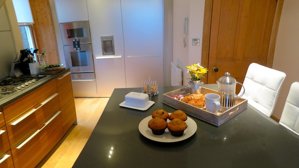 A modern kitchen with a wooden countertop, a coffee maker, a tray with pastries, and a plate of muffins. - Inverleith Estate (Edinburgh)