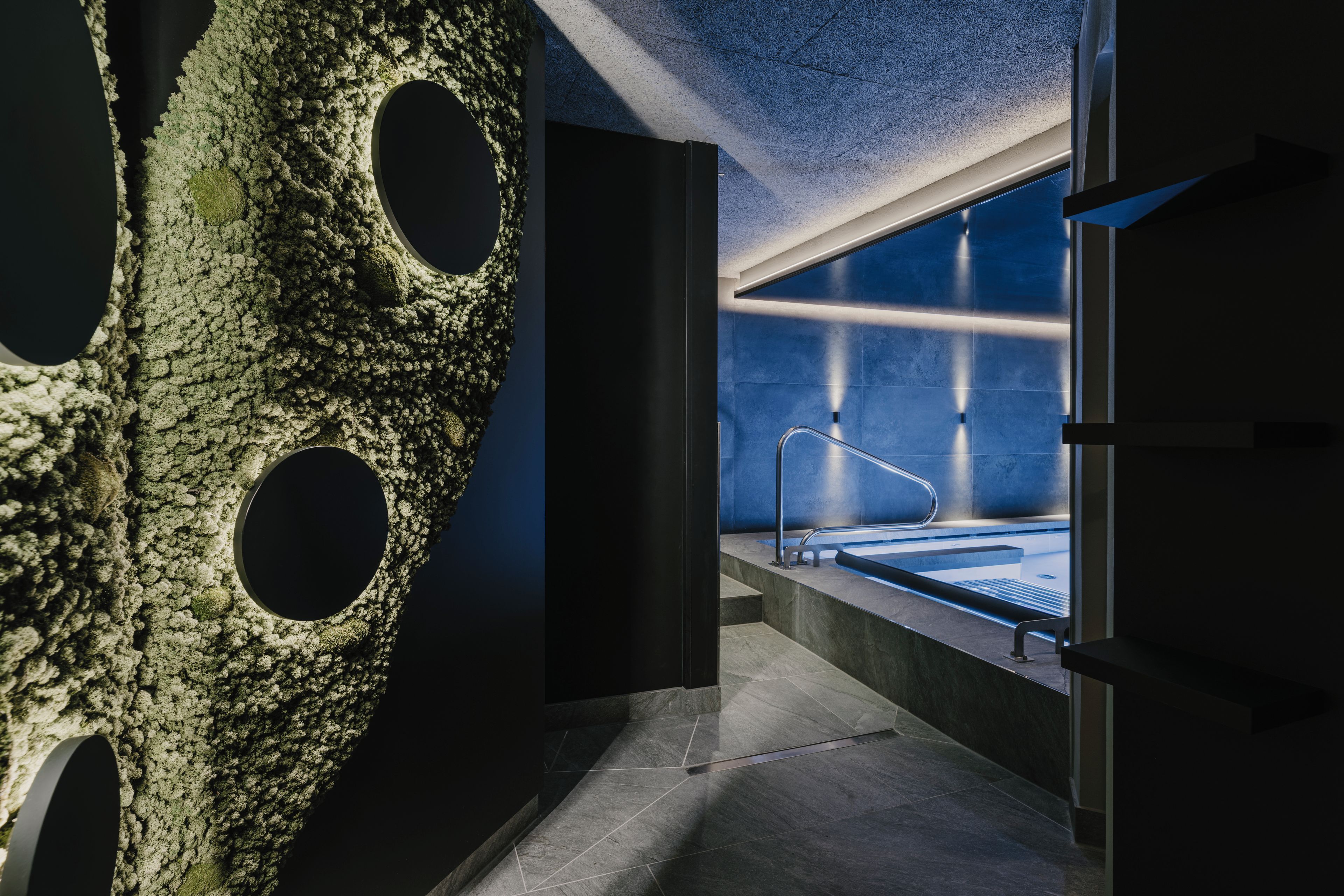 Un baño moderno con una pared grande y texturizada, una bañera a la vista y un separador de vidrio.