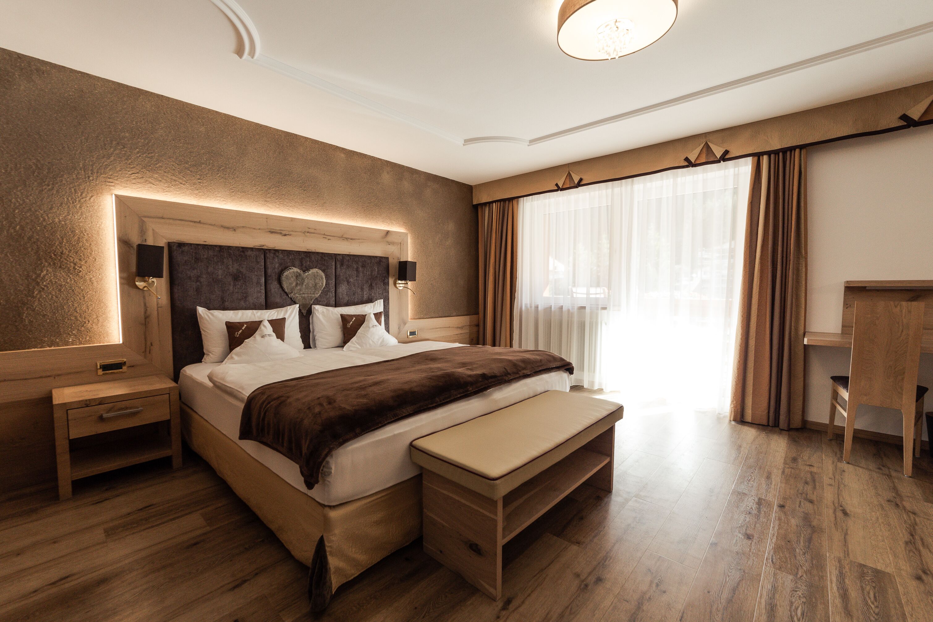 Een moderne slaapkamer met een houten bed, nachtkastjes, een bankje en een bureau.