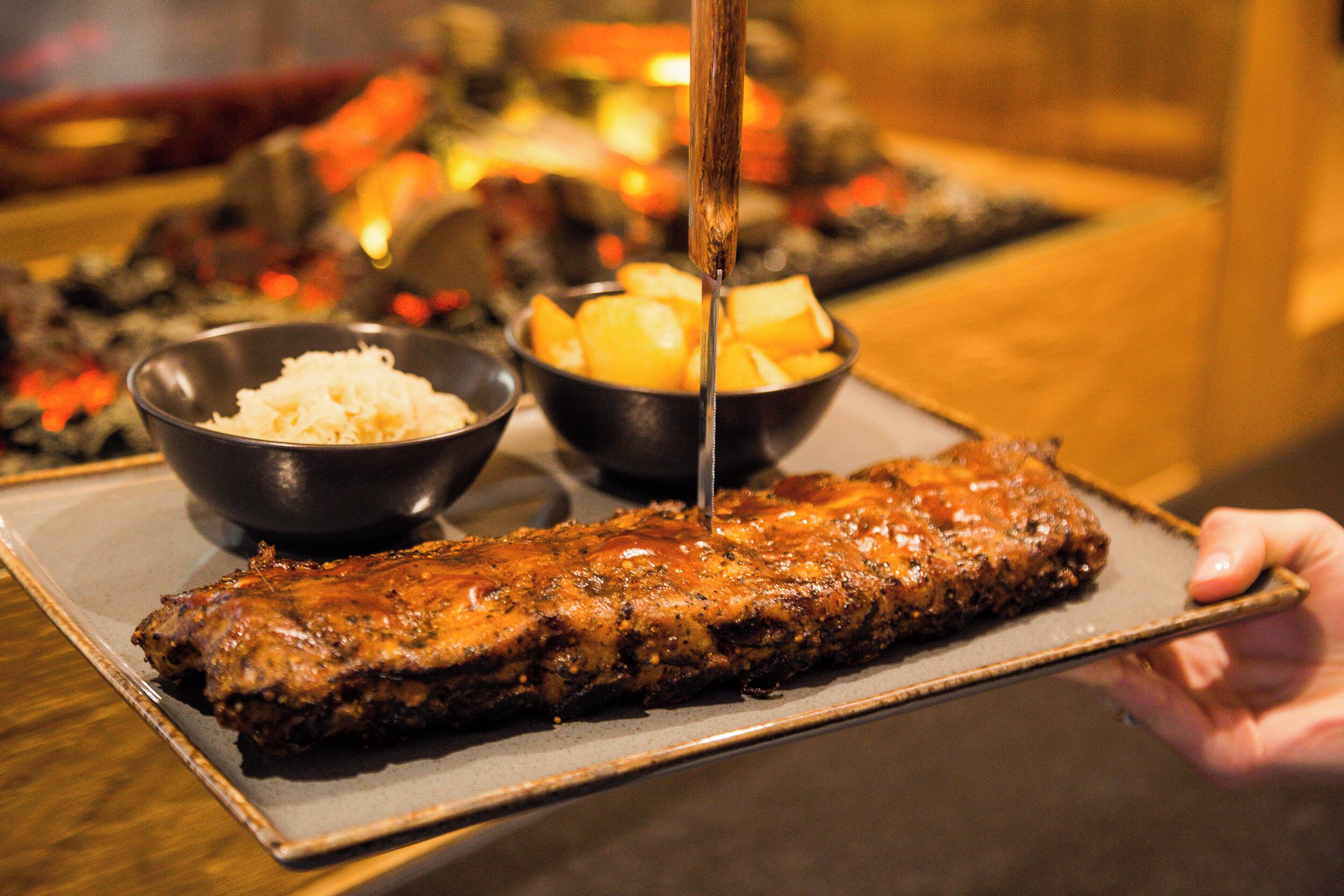 Una persona sostiene una bandeja con un plato de carne cocinada, acompañado de un tazón de arroz y un tazón de papas.