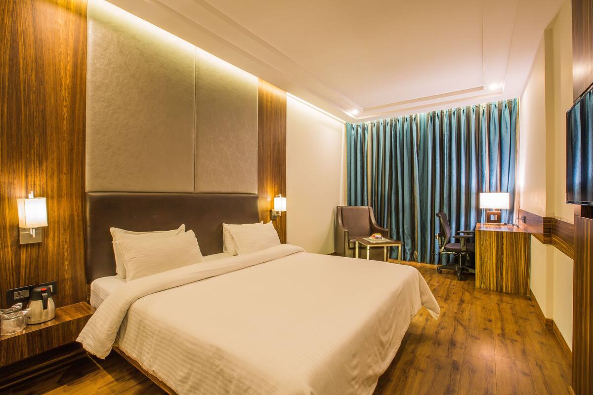 A hotel room with a large bed, a desk, a chair, and a television.