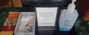 A hotel room with a hand sanitizer dispenser, a thermometer, a bottle of hand soap, and a menu. - Hotel Hemala (Karur)
