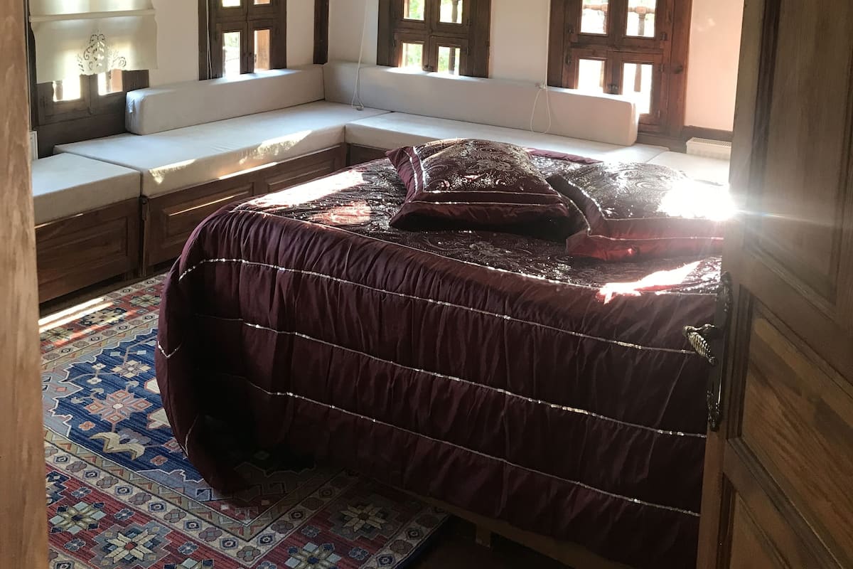 Une chambre avec un grand lit, un plafond en bois et un coin fenêtre agrémenté de rideaux.