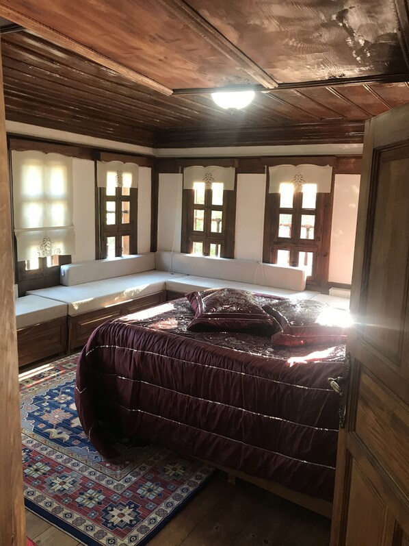 A bedroom with a large bed, wooden ceiling, and a window seat with curtains.