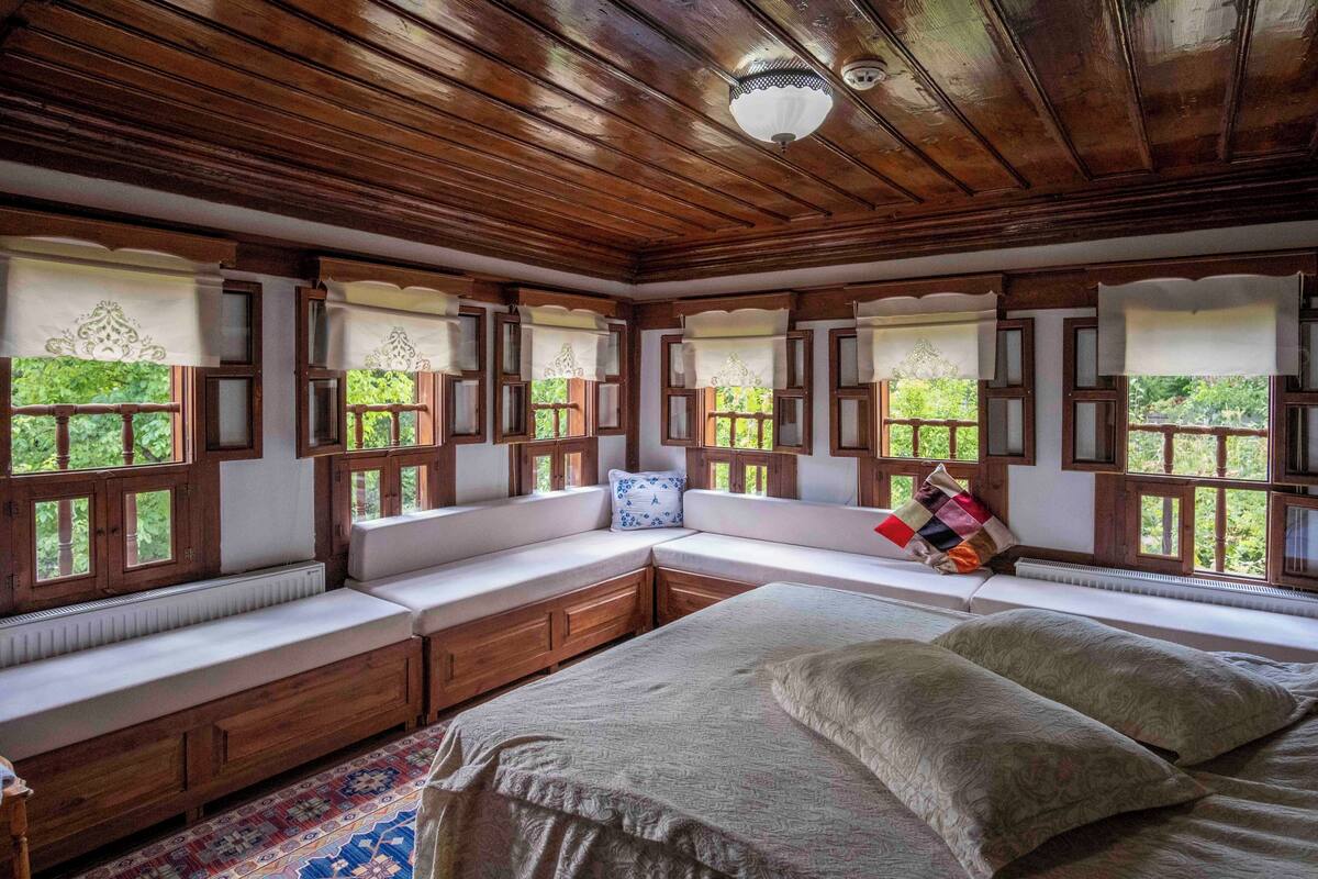 Une pièce dotée d’un grand lit, d’un plafond en bois et de banquettes intégrées le long des fenêtres.