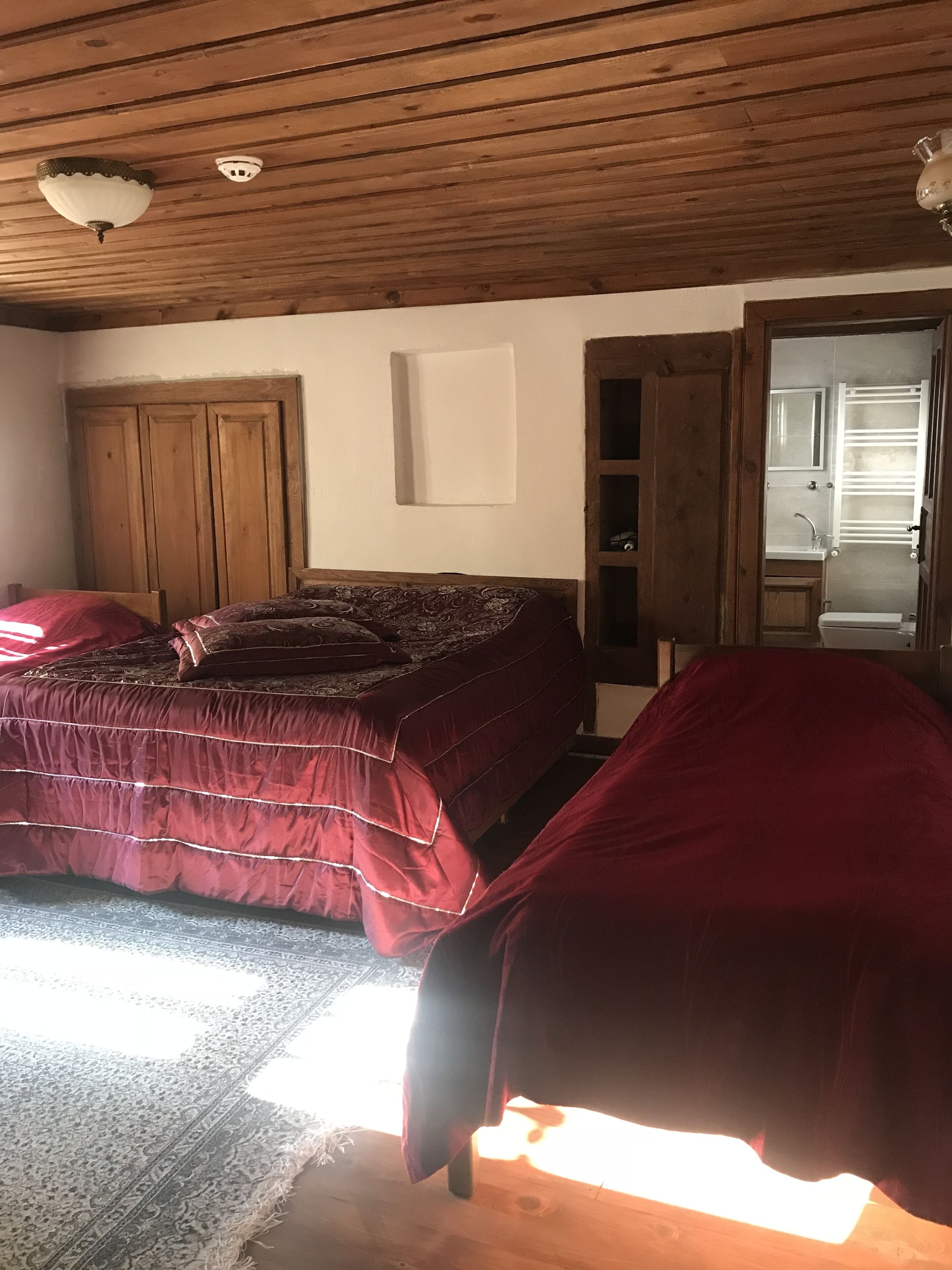 Ein Schlafzimmer mit einem großen Bett, einem Holzschrank, einem Nachttisch und einem durch eine offene Tür einsehbaren Badezimmer.