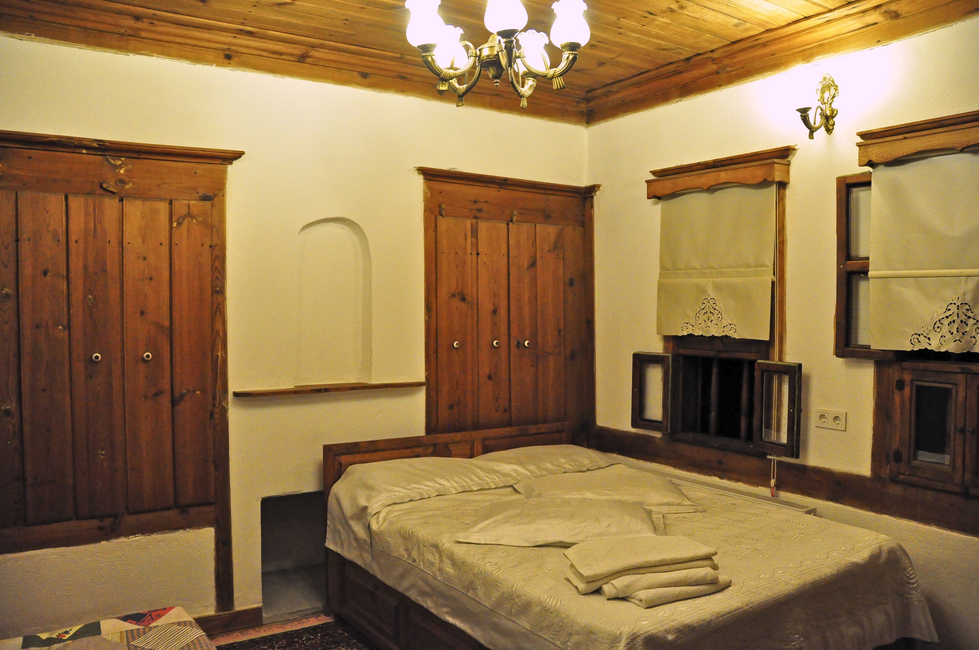 A bedroom with wooden wardrobes, a bed with a beige bedspread, and a mirror with a decorative frame.