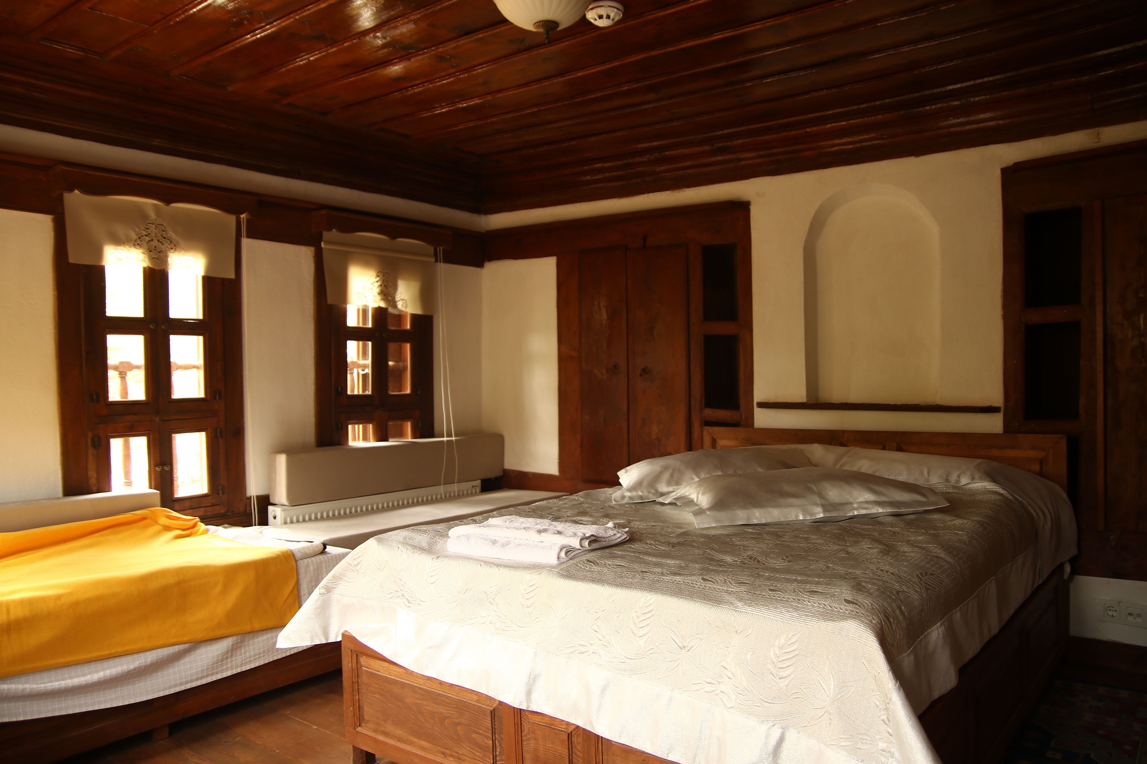 Una habitación con dos camas, techo de madera y ventana con cortinas.