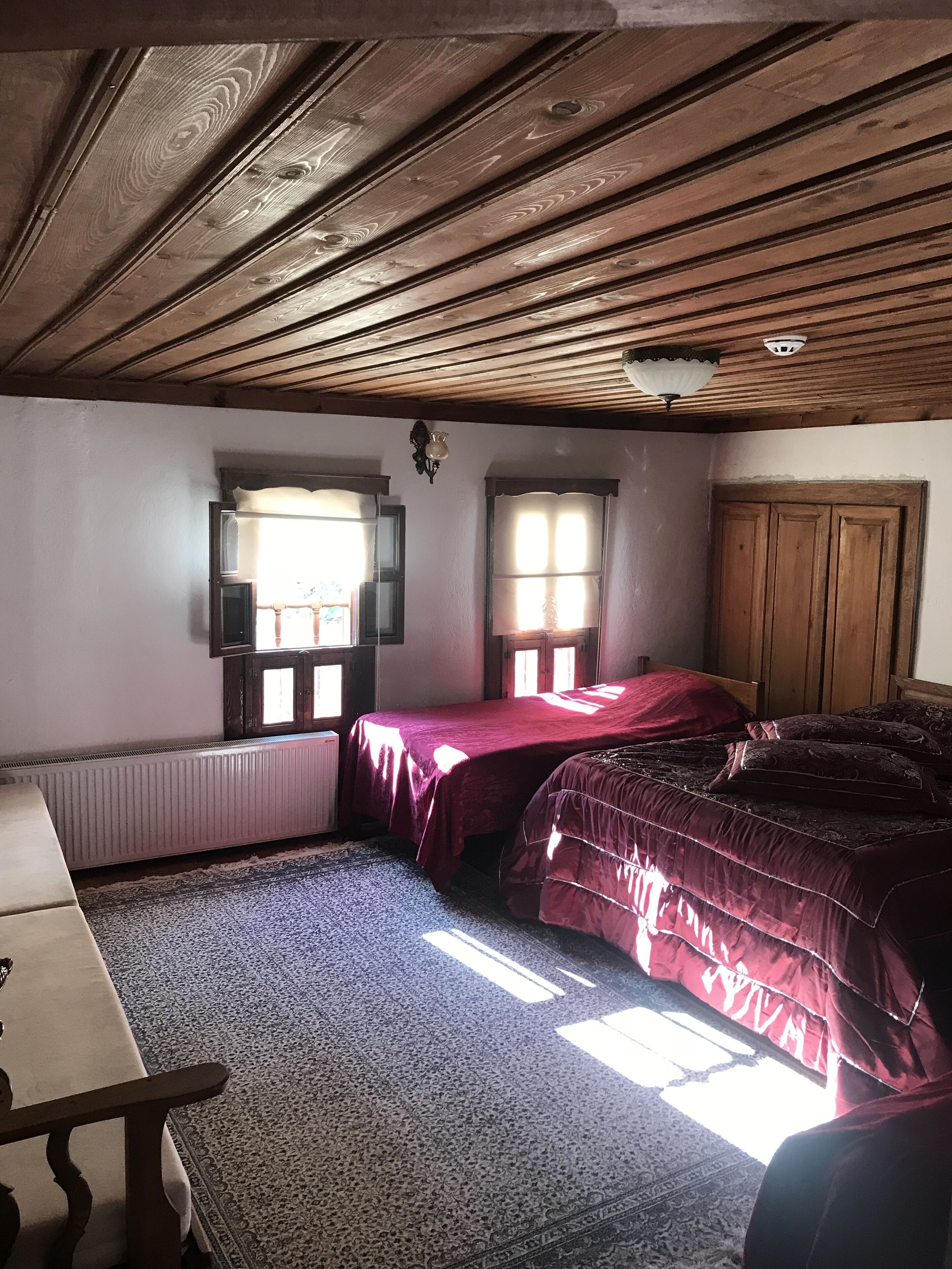 A bedroom with two beds, a radiator, a window, and a wooden ceiling.