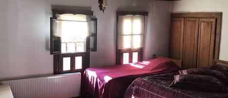 A bedroom with two beds, a radiator, a window, and a wooden ceiling.