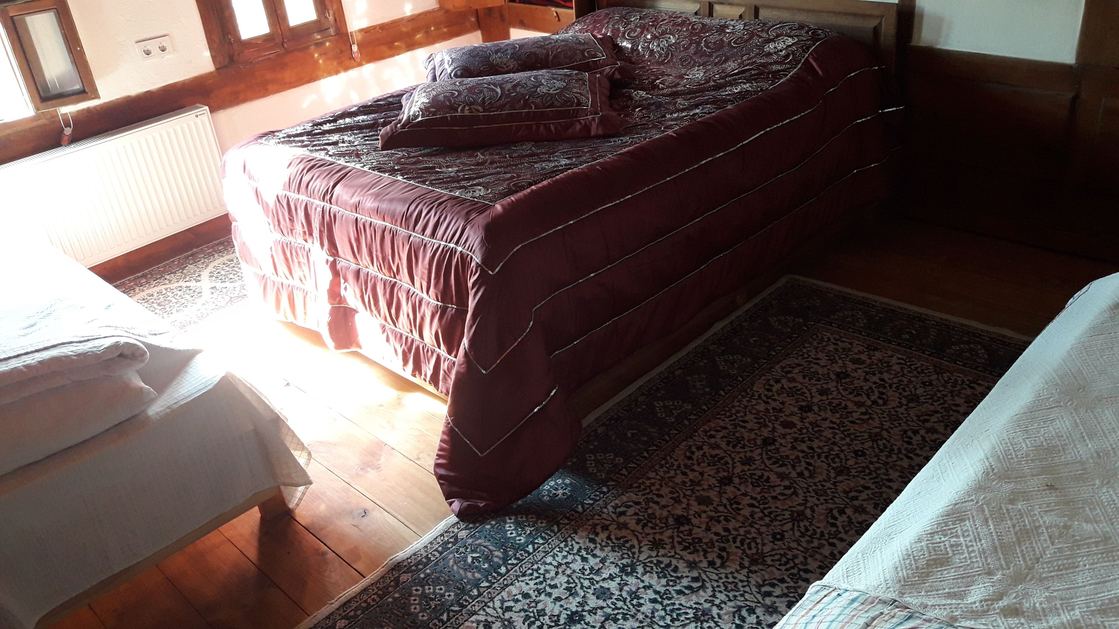Uma cama com colcha e almofadas estampadas, piso de madeira e tapete estampado.
