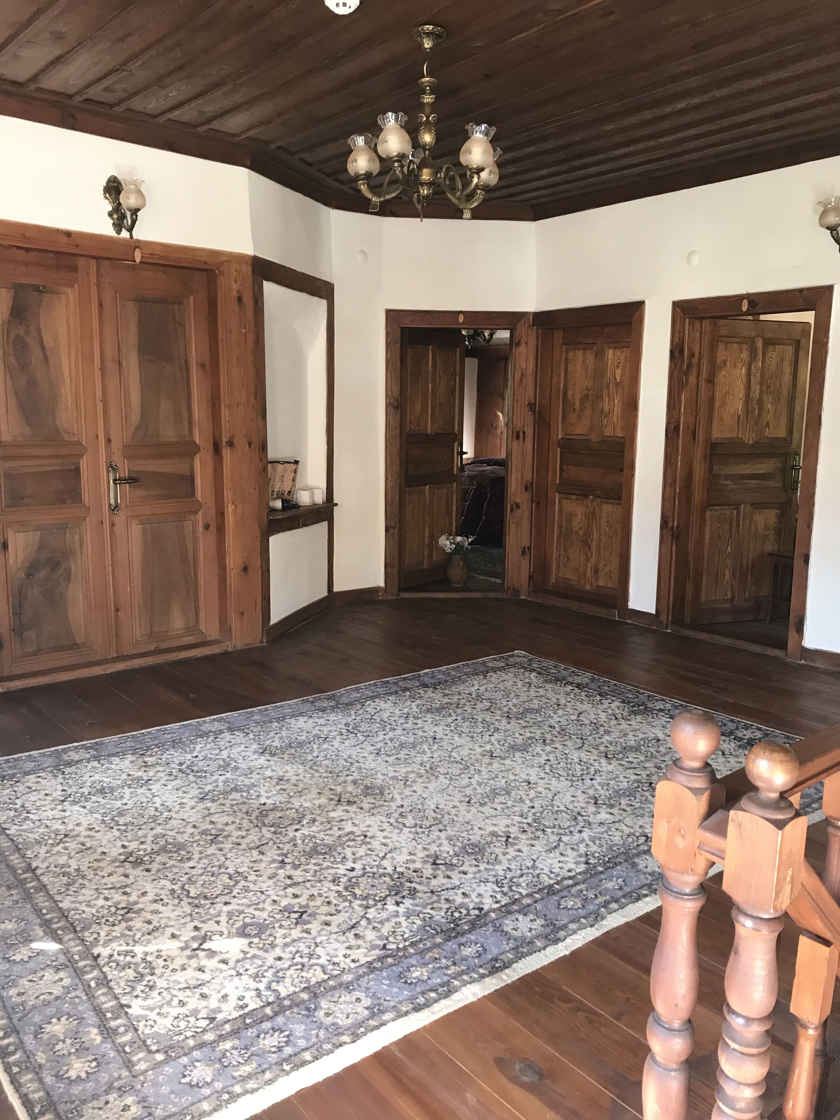 Een ruime kamer met houten vloeren, een groot tapijt met dessin en een houten trap met balustrade.