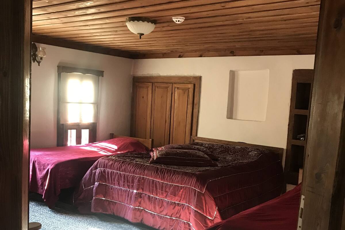 Une chambre avec deux lits, des poutres apparentes en bois au plafond, une fenêtre avec des rideaux et une armoire en bois.
