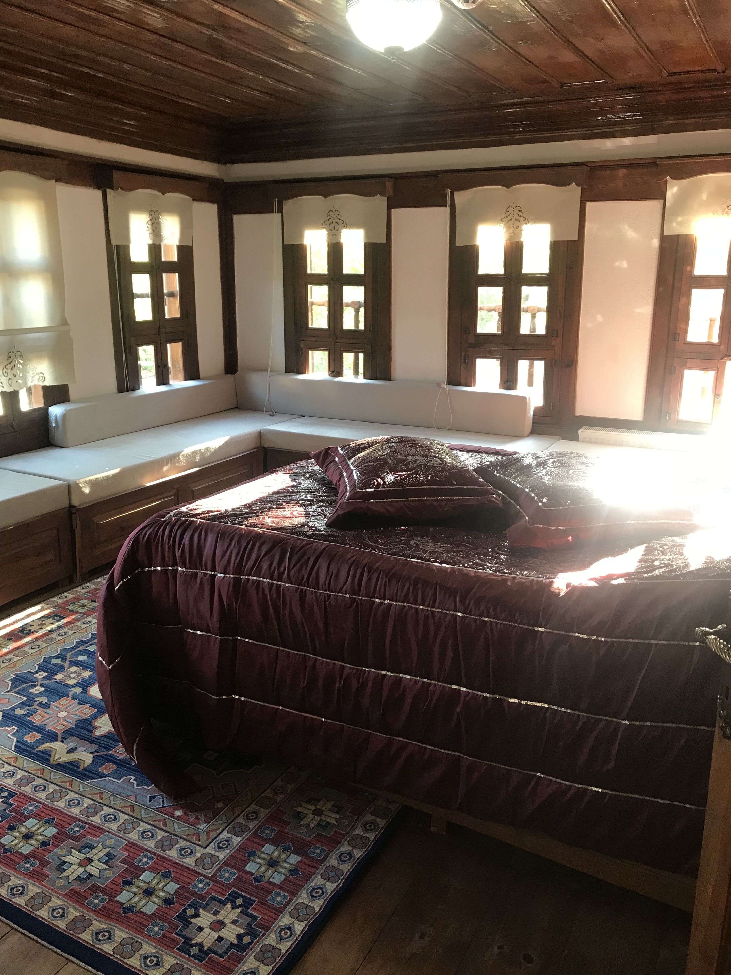 A room with a large bed, wooden beams on the ceiling, and a bench with a view of the outdoors.