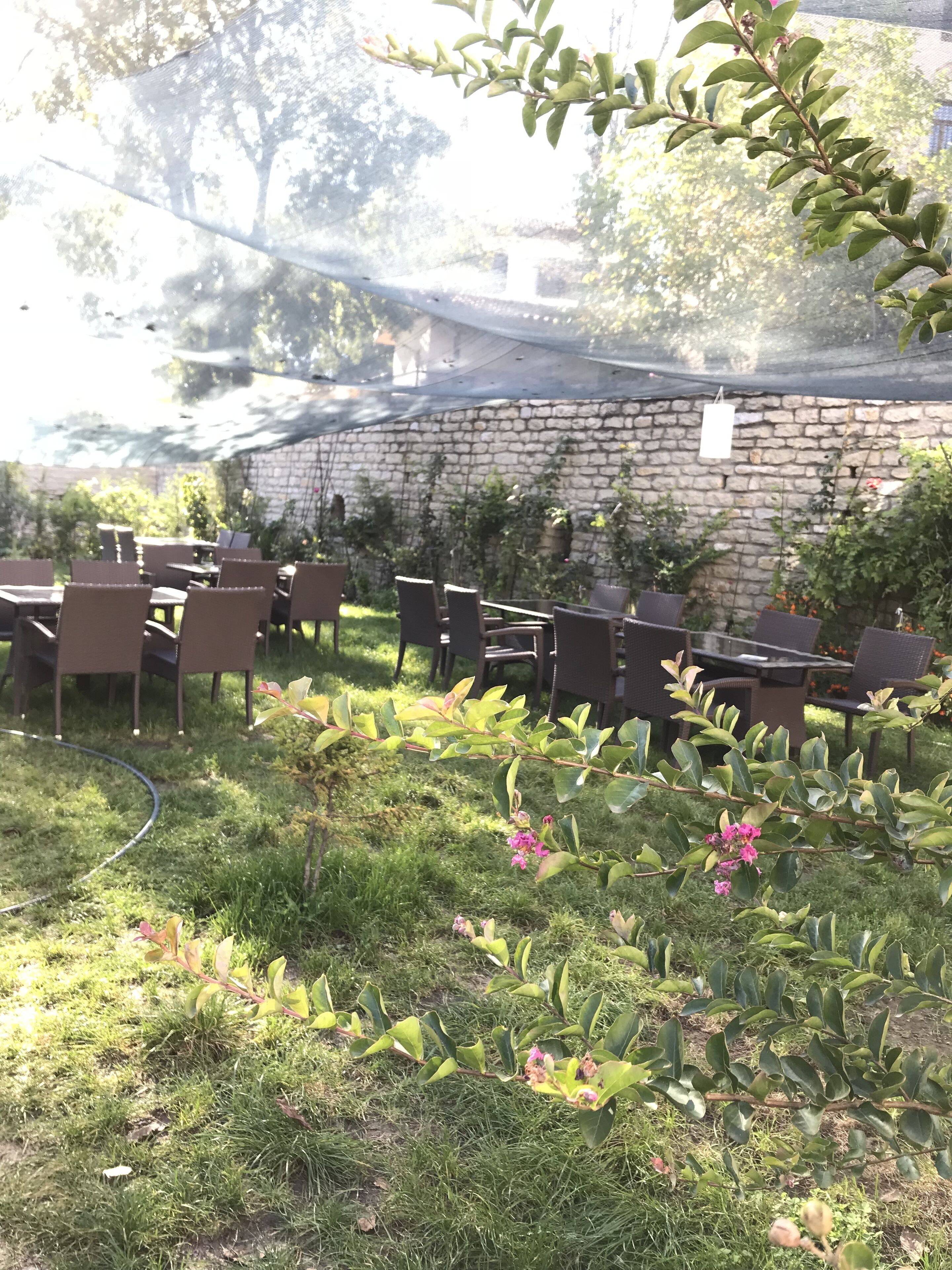 An outdoor seating area with tables and chairs, surrounded by a stone wall and greenery.