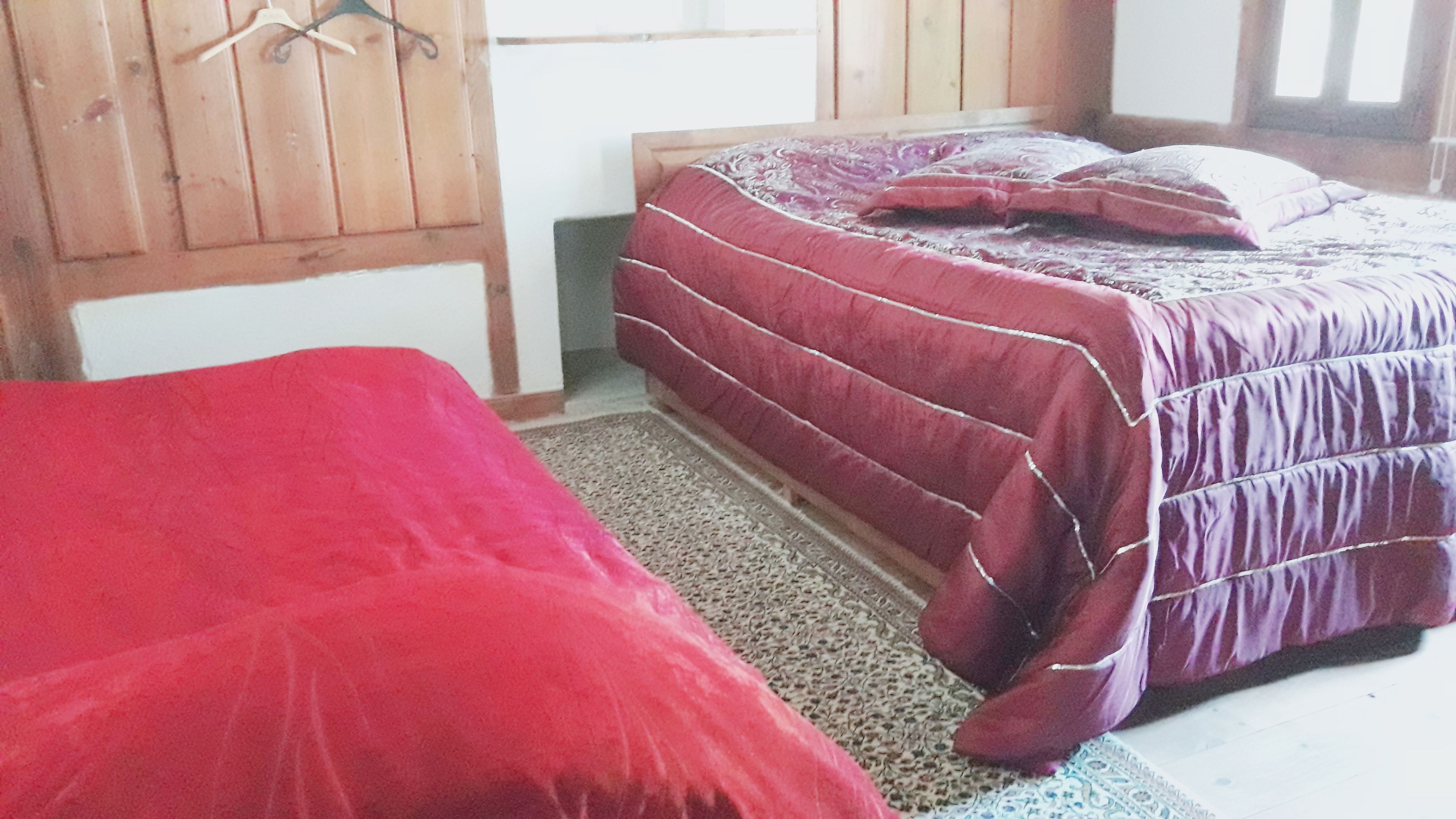 A bedroom with a bed covered in a red blanket, a wooden headboard, and a patterned rug.