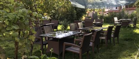An outdoor patio area with tables and chairs, surrounded by greenery and a protective netting.