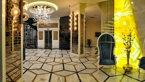A lobby with a geometric tile floor, two blue armchairs, a glass table, and a decorative chandelier. - Exelans Hotel (Fethiye)